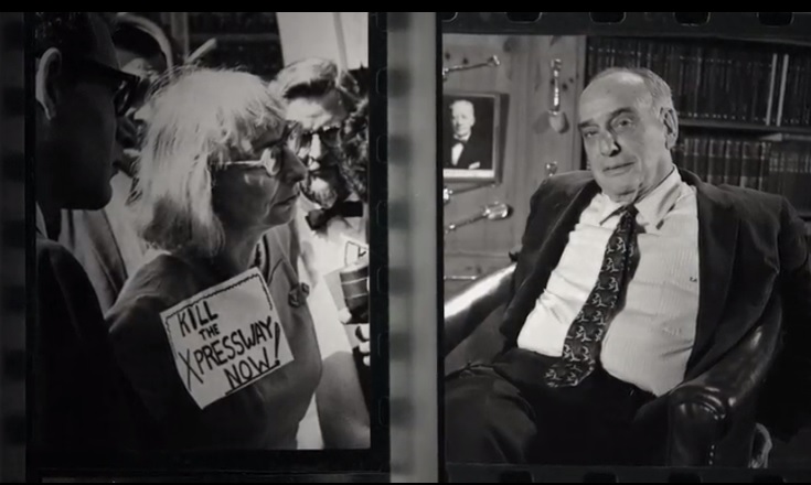 An older woman with white hair is outside a closed office door carrying a sign that says, "Kill the Xpressway Now!" A weary older man inside the office looks at the camera.