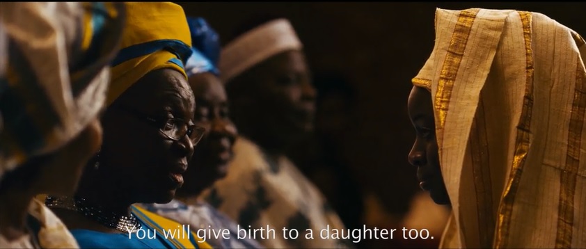 An older woman in a traditional Nigerian hat telling a young woman, "You will give birth to a daughter too."