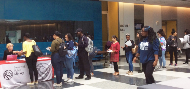 A long line of John Jay students in front of a table with NYPL branding