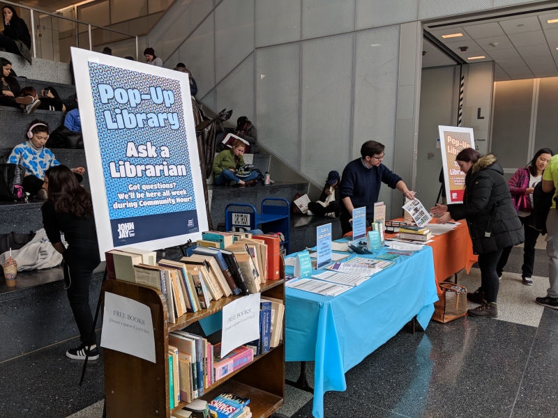 Tables, students, and librarians, with sign that says Pop Up Library: Ask A Librarian